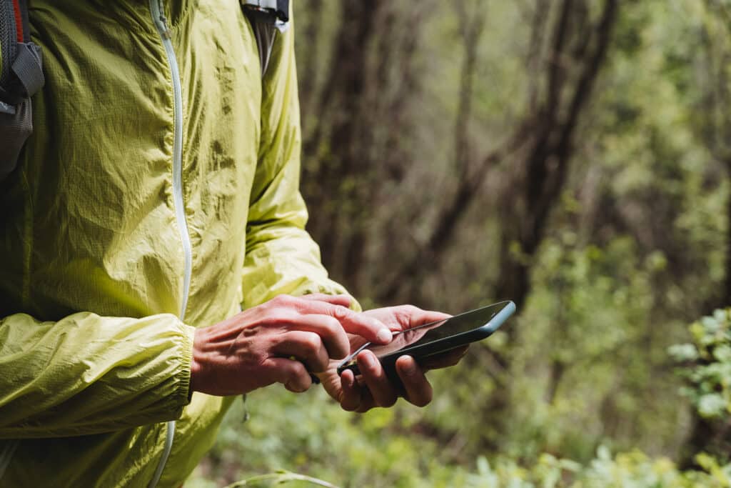 The phone lies in the hand of a person, typing with a finger on a smartphone, cellular communication in the forest, the use of gadgets on a hike\. High quality photo